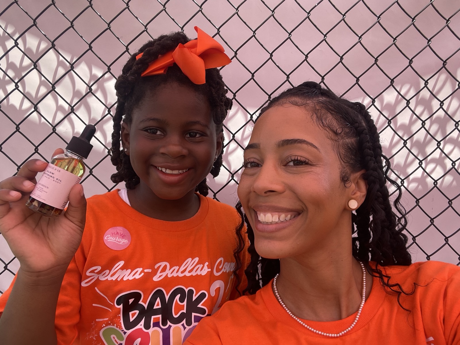 Ella smiling with a young participant in an orange Back 2 School shirt who holds up a product