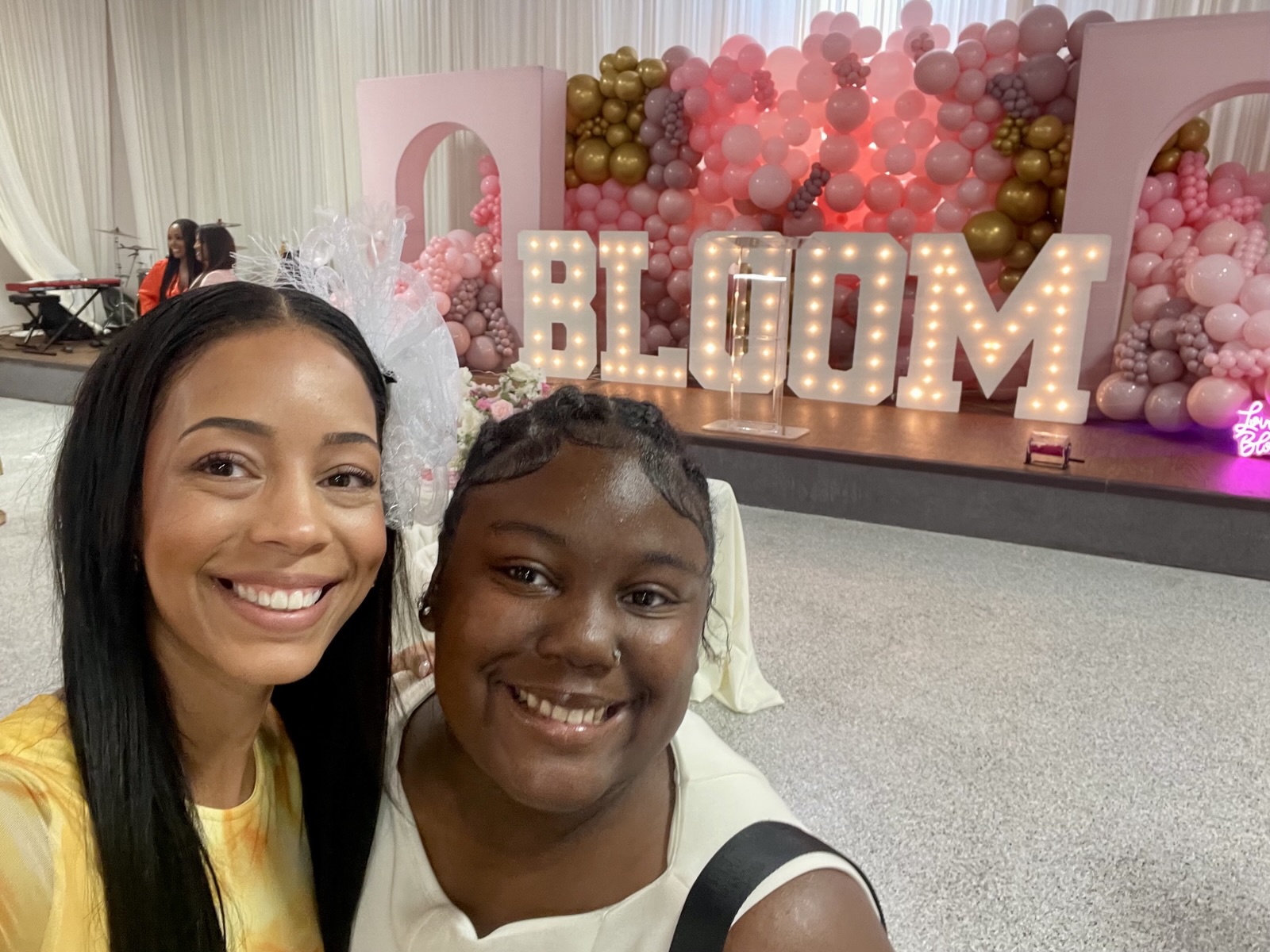 Ella Alexandria Love smiling beside a young woman in front of lit-up BLOOM letters