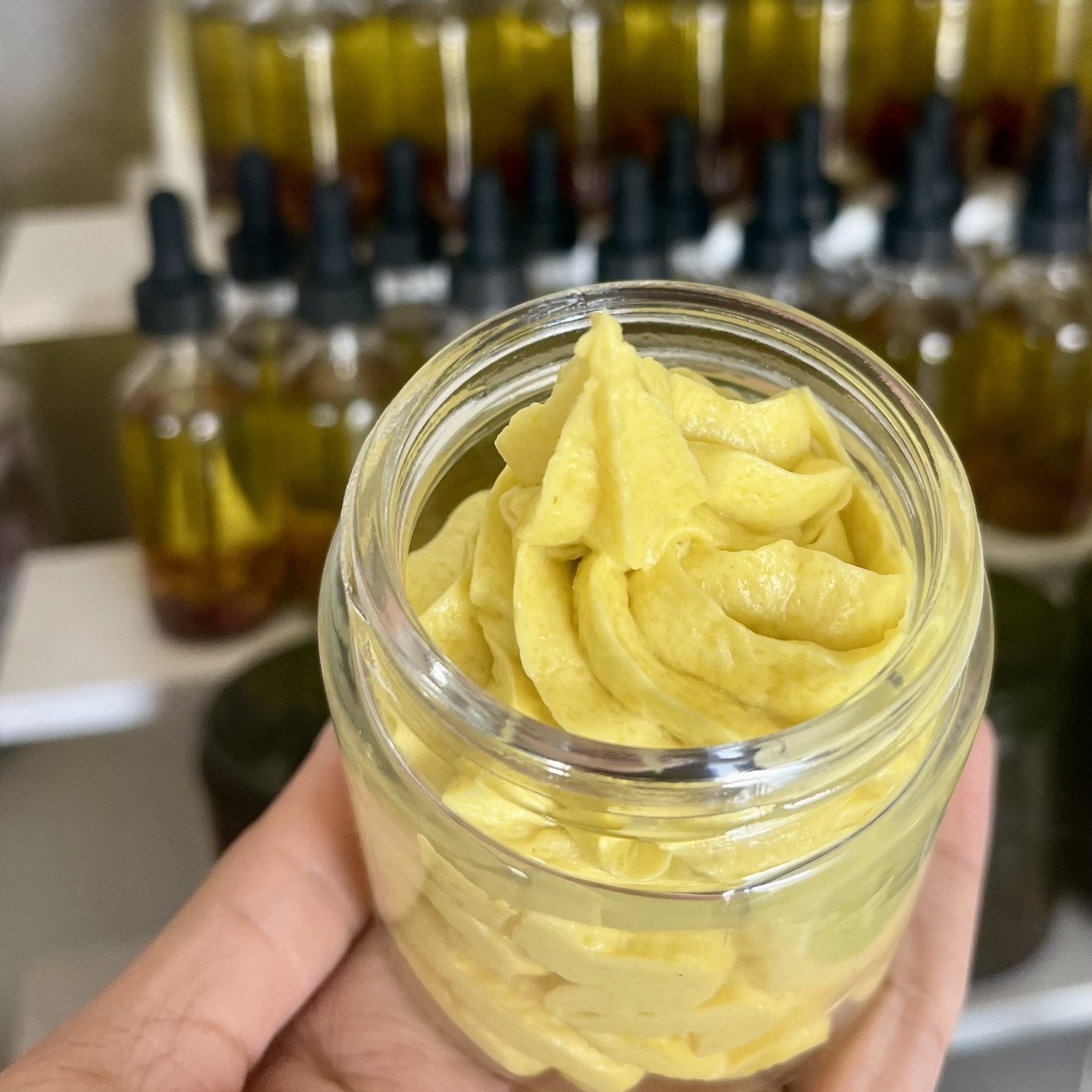 A hand holding an open jar of whipped body butter made in the Angelic & Co. Studio