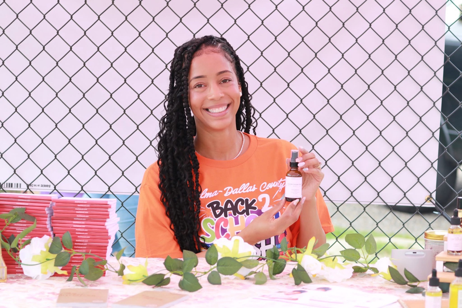 Ella at an outdoor booth holding up a bottle of product