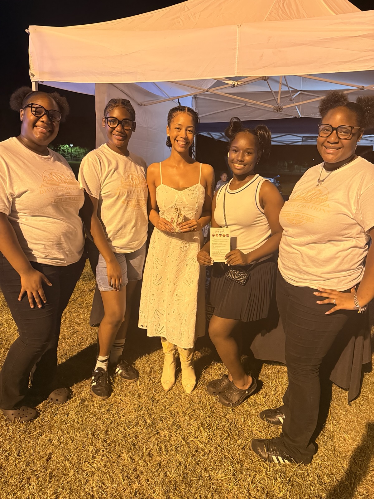 Ella with four young people in white under a tent at an evening community event