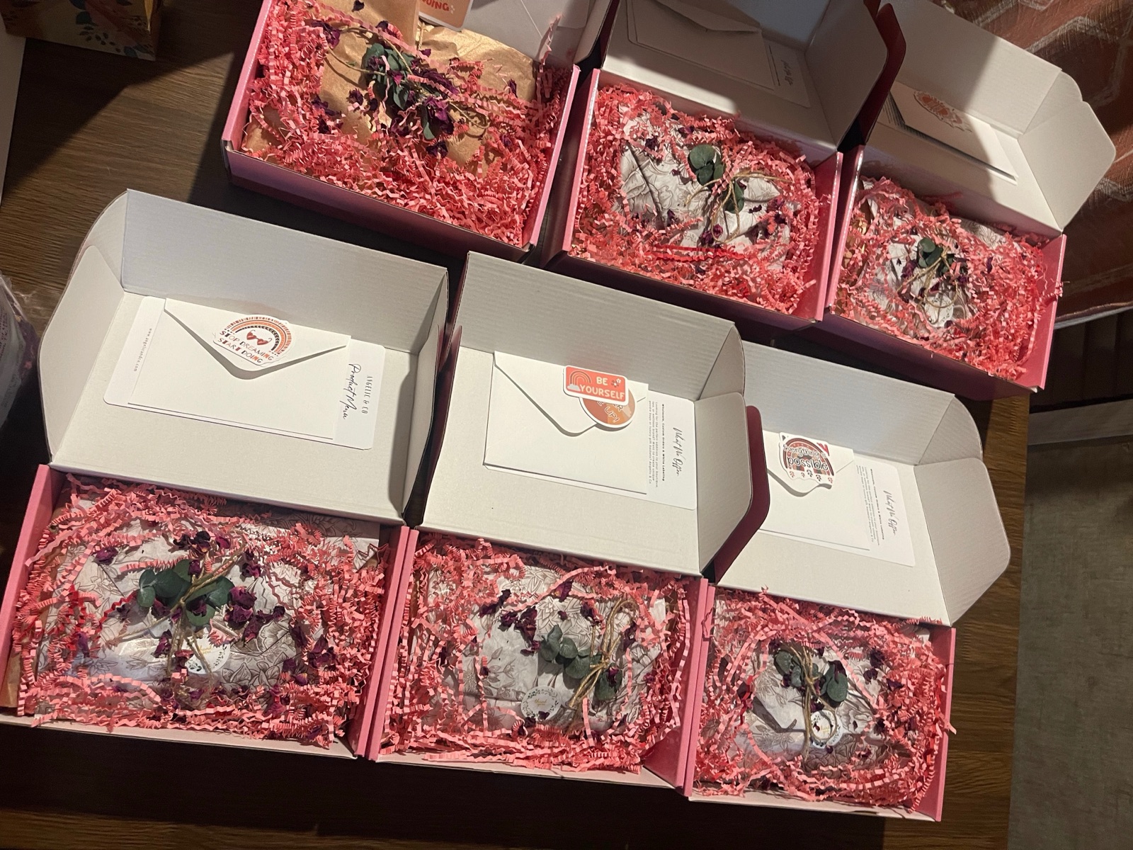 Open gift boxes lined with pink crinkle paper, each holding a packaged product