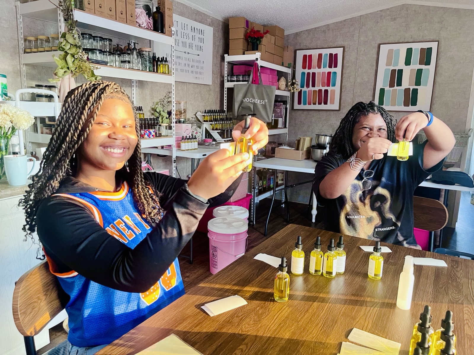 Two young women smiling and holding up small bottles of product they prepared in the Angelic & Co. workshop