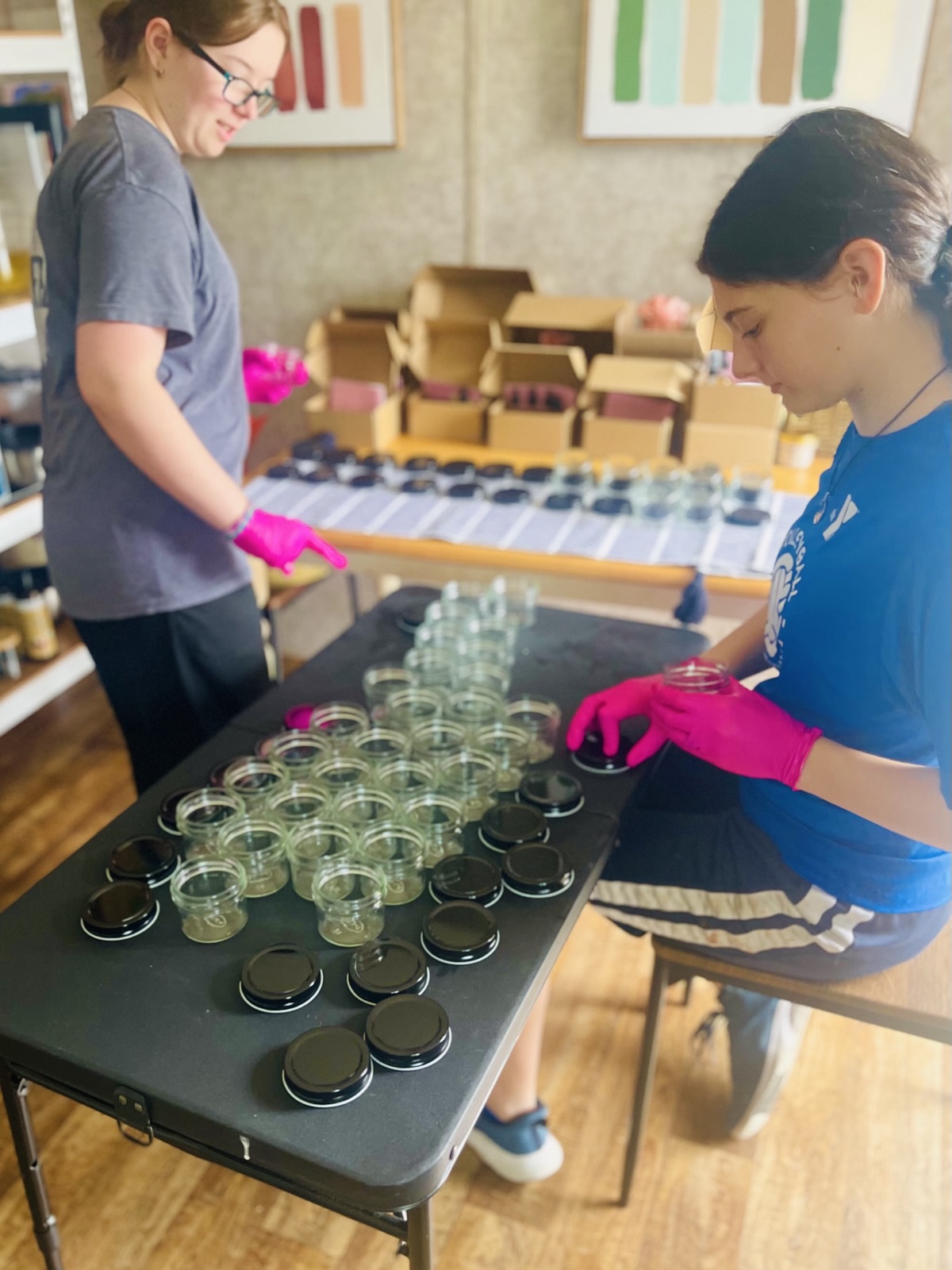 Two participants preparing rows of product jars on a studio worktable