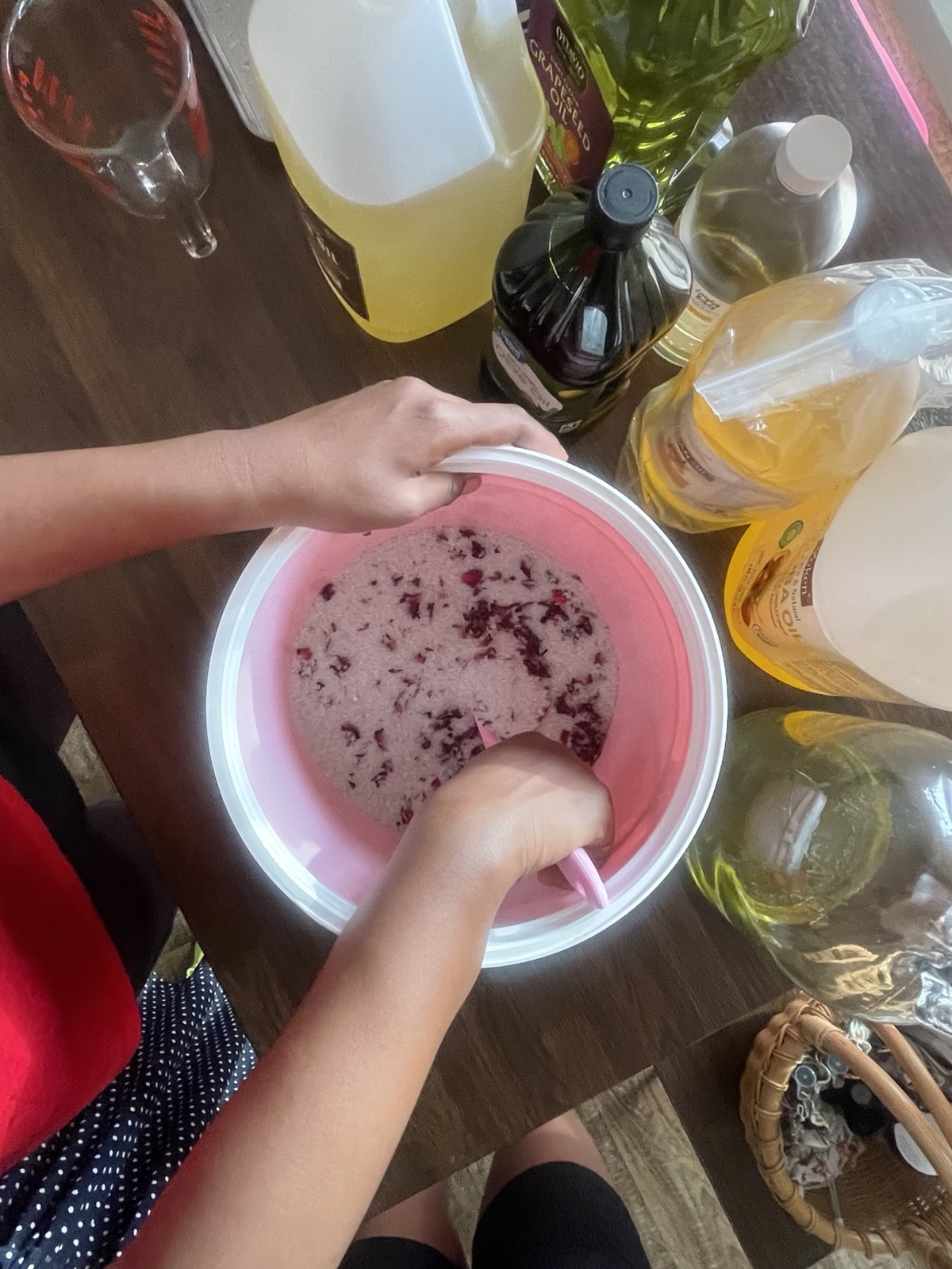 Hands stirring a pink mixture with dried petals in a bowl